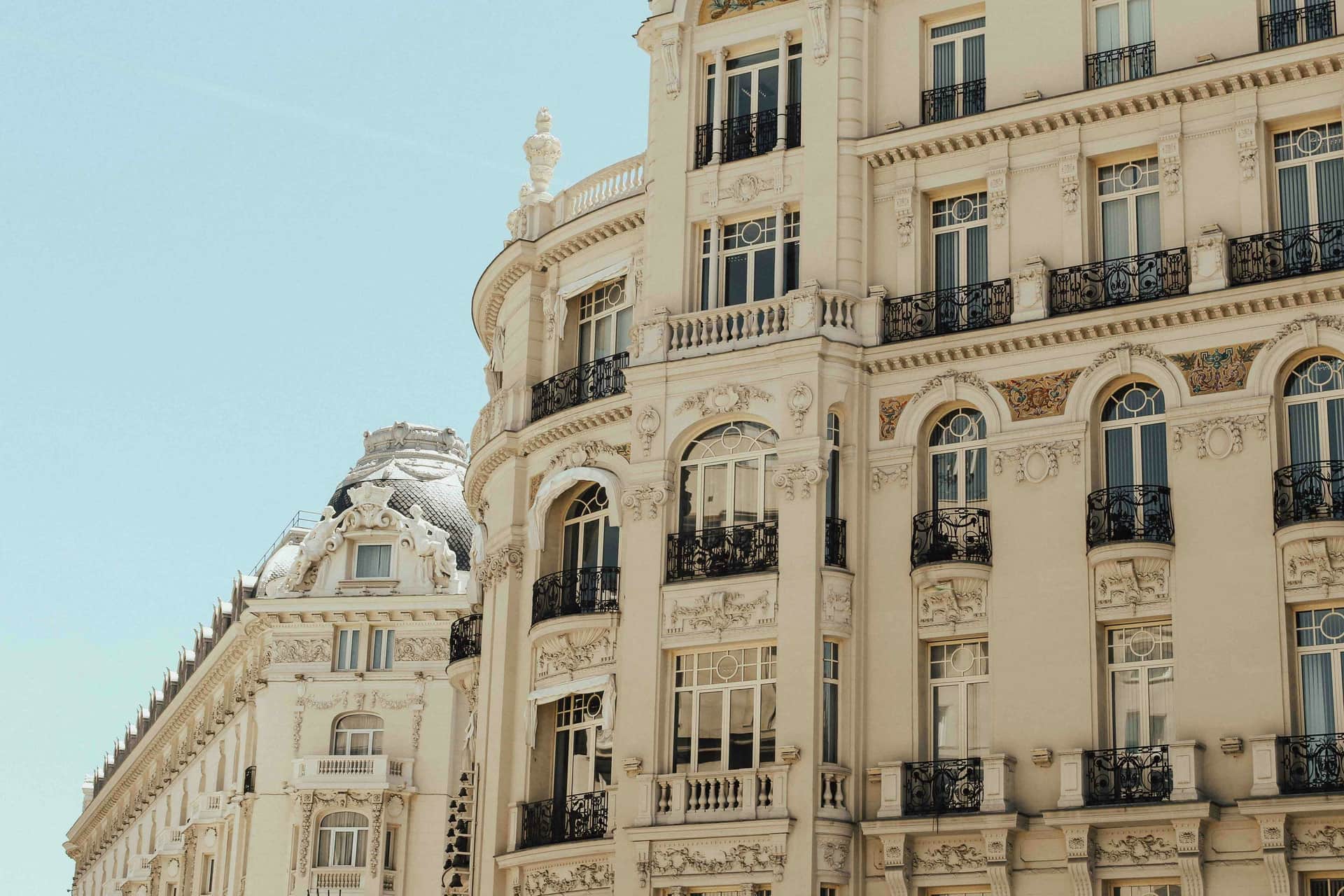 Fachada de un edificio histórico señorial en Madrid, piedra color crema con balcones de hierro forjado bajo un cielo azul despejado